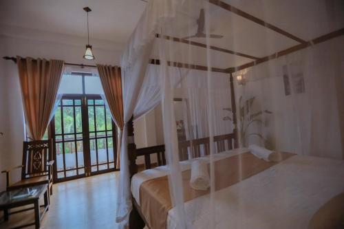 a bedroom with a canopy bed with a window at Nibbana Mirissa Hotel in Mirissa