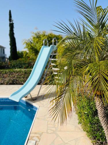 a blue slide next to a swimming pool with a palm tree at Villa Amandine in Peyia