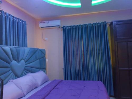 a bedroom with a bed with a blue headboard and curtains at 2 Bed-Sleeps 4-Free Parking-AirCon in Benin City