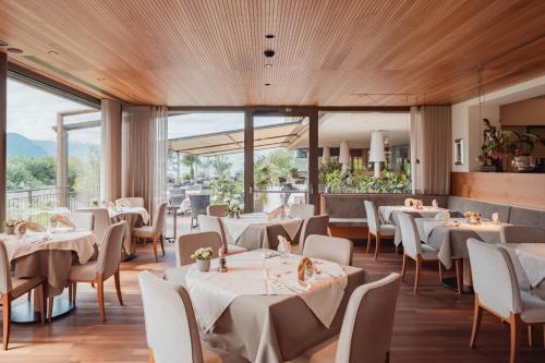 a restaurant with white tables and chairs and large windows at Hotel Girlanerhof in Appiano sulla Strada del Vino