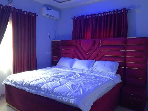 a bedroom with a large bed with red curtains at 2 Bed-Sleeps 4-Free Parking-AirCon in Benin City