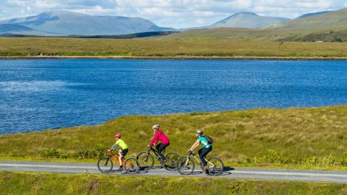 three people riding bikes down a road near a lake at Achill Island Holiday home by the Sea in Achill Sound