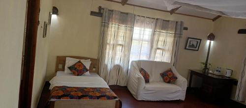 a bedroom with a bed and a chair and a window at Kilimanjaro Lodge Cabins in Moshi