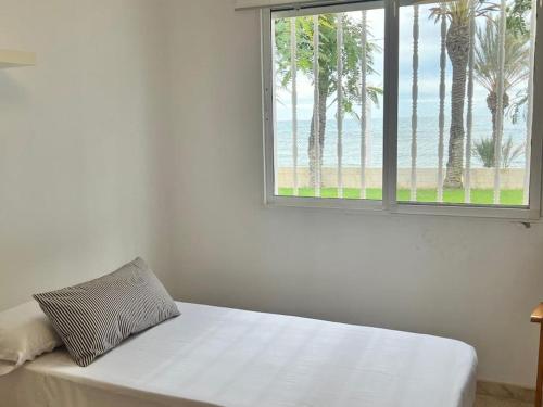 a bedroom with a bed with a window with palm trees at Triana II, Primera línea de mar, La Azhoía in Cartagena