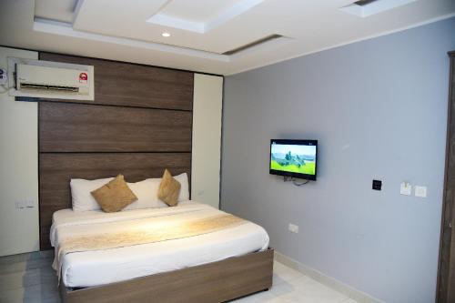 a bedroom with a bed with a tv on the wall at Hotel De Alommah Kubwa Abuja in Abuja