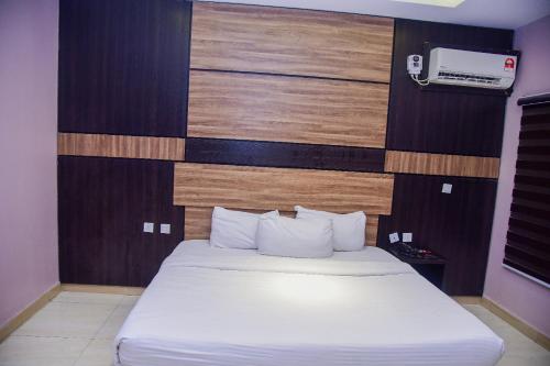 a bedroom with a white bed with a wooden wall at Hotel De Alommah Kubwa Abuja in Abuja
