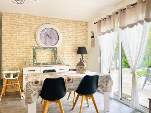 a dining room with a table and a clock on the wall at Petite maison au calme in Poupry