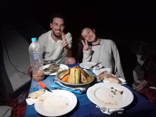 a man and a woman sitting at a table with food at Canadien camp merzouga in Merzouga