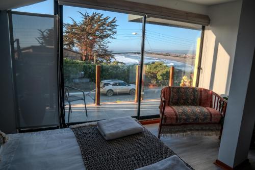 a bedroom with a bed and a chair and a large window at Hotel Boutique Aldea del Mar in Pichilemu