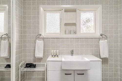 a white bathroom with a white sink and two windows at Charming Blue Mountains Cottage Katoomba in Katoomba