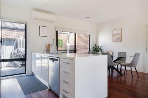 a kitchen with white cabinets and a dining room with a table at 'The Leon' A Family Friendly Coastal Abode in Rosebud