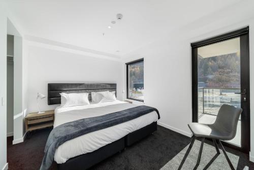 a white bedroom with a large bed and a chair at Residence du Parc - Luxury Apartment in Queenstown