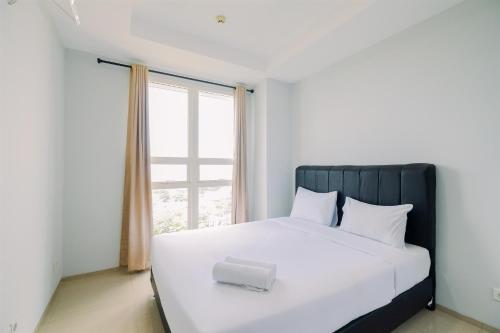 a white bed with a black headboard and a window at Best Choice and Restful 1BR CitraLake Suites Apartment By Travelio in Jakarta