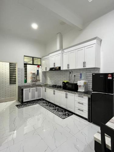 a kitchen with white cabinets and a black refrigerator at POKMA Homestay in Kampong Molek