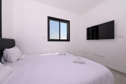 a white bedroom with a white bed and a television at לוי-קיישן מגוון דירות גן ופנטהאוזים וסוויטות נוף ברחוב הצנחנים in Tiberias