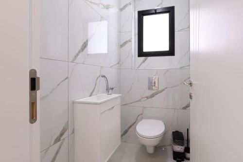 a white bathroom with a toilet and a window at לוי-קיישן מגוון דירות גן ופנטהאוזים וסוויטות נוף ברחוב הצנחנים in Tiberias