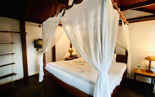 a bedroom with a canopy bed with white curtains at Village Susegat Beach Resort in Morjim