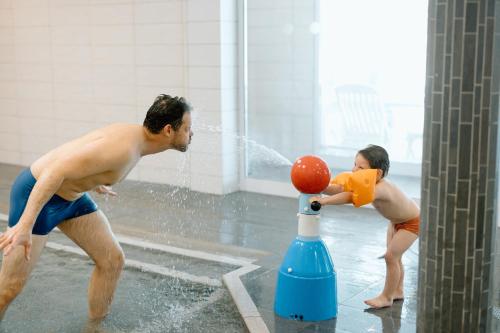 un homme et un garçon jouant avec un ballon dans une fontaine dans l'établissement Résidence b'o cottage - b'o resort thermal & spa, à Bagnoles-de-l'Orne