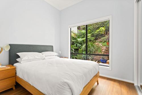 a white bedroom with a bed and a window at Bea's Cottage in Clontarf in Sydney