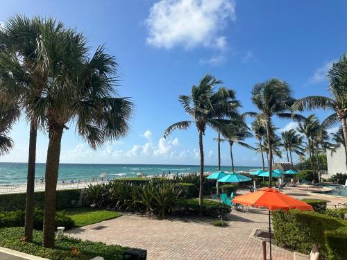 a beach with palm trees and an orange umbrella at Amazing beachfront condo at Tides on Hollywood Beach Luxury Resort in Hollywood