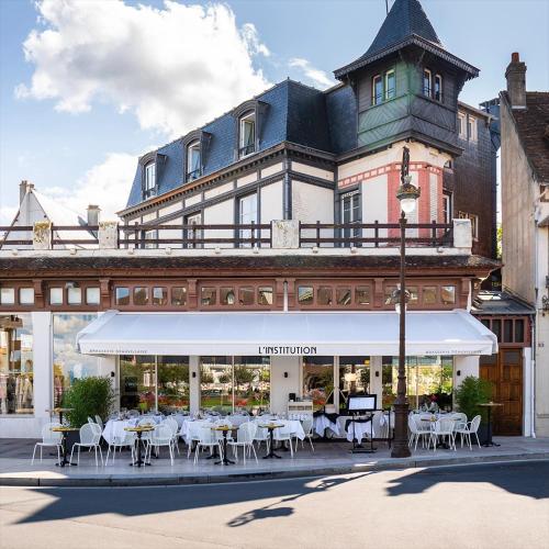 un bâtiment avec des tables et des chaises devant lui dans l'établissement En face de l'hôtel Normandy - Appartement dernier étage, à Deauville