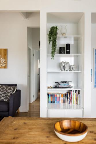 a living room with a table and a book shelf at Orion Beach Cottage A - Jervis Bay in Vincentia