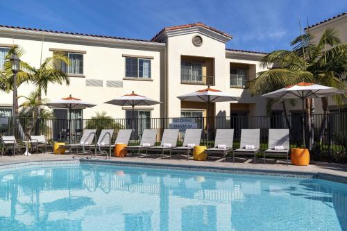 a pool with chairs and umbrellas in front of a hotel at Courtyard by Marriott Santa Barbara Goleta in Santa Barbara