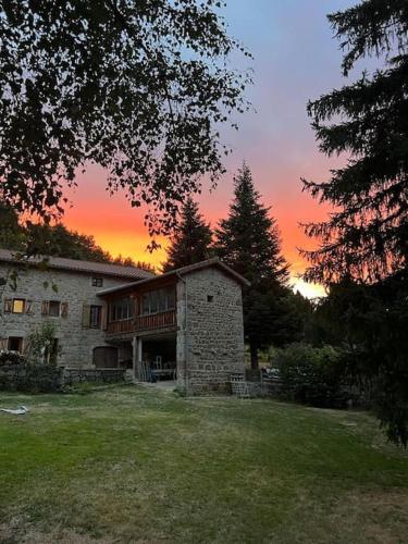 a large stone house with a sunset in the background at Maison de caractère in Viverols