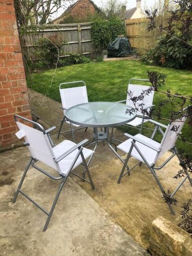 three chairs and a glass table in a yard at Beautiful Cotswold Couples Retreat in Bourton on the Water