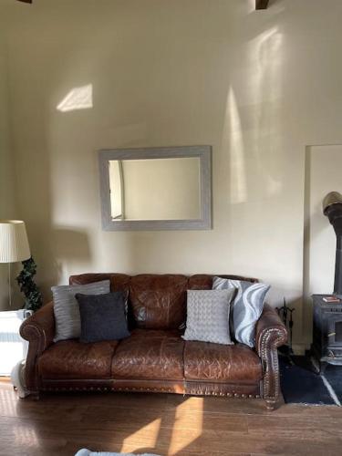 a brown leather couch in a living room with a mirror at Beautiful Cotswold Couples Retreat in Bourton on the Water