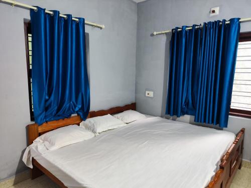 a bedroom with two beds with blue curtains at Brahmagiri Homestay Serviced Villa in Thirunelli