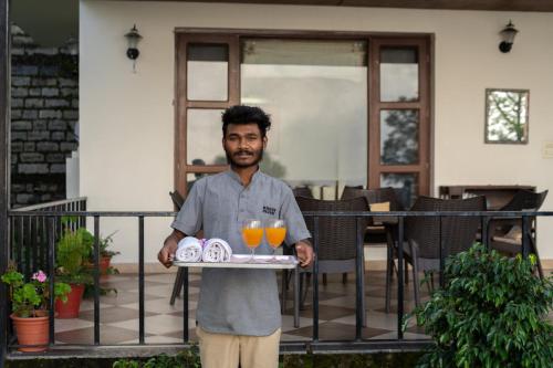a man holding a tray with two glasses of orange juice at StayVista at The Haven in Kasauli