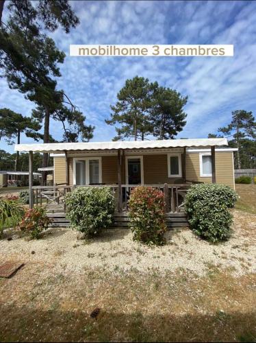 une petite maison avec une terrasse couverte et des buissons dans une cour dans l'établissement Mobil home 3 chambres ACM, à Vendays-Montalivet