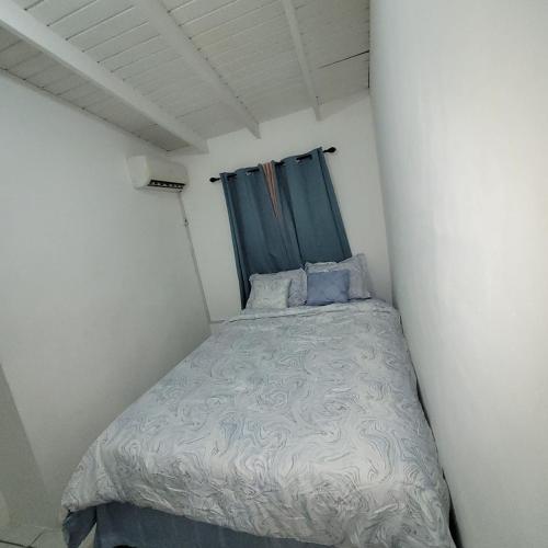 a bed in a small room with blue curtains at ADA APARTMENTS Saint Lucia in Castries