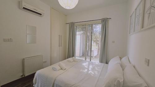 a white bedroom with a bed with white sheets and a window at STAY Pantheon Villa in Pissouri