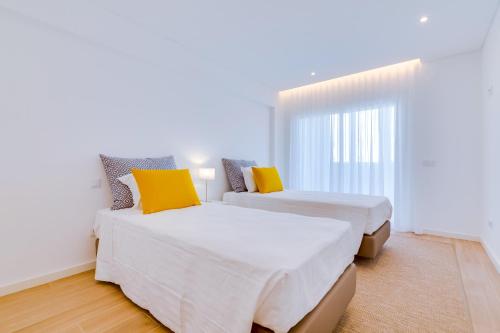 two beds in a white room with yellow pillows at Apartamento Gaivota frente-mar in Quarteira