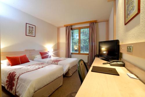 a hotel room with two beds and a desk with a television at Le Bois Dormant-Hôtel Restaurant & Spa Logis Hôtel in Champagnole