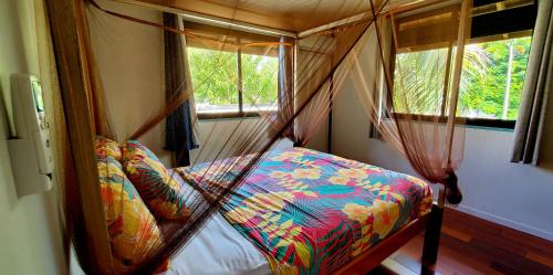 a bedroom with a canopy bed with two windows at Fare Haumaru in Teavaro