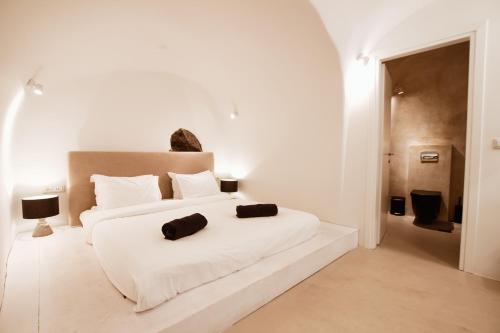 a white bedroom with a white bed with two black towels on it at Kaleidoscope Cave Houses in Oia