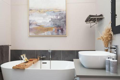 baño con bañera blanca y una pintura en la pared en HERON COTTAGE - for your seaside holiday., en Chintsa
