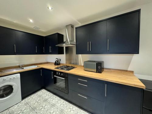 a kitchen with dark blue cabinets and a microwave at Zetland House Apartment - First floor with garden and parking in Southport