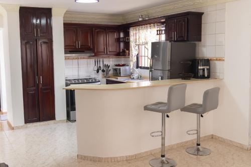 a kitchen with wooden cabinets and a counter with two stools at Residencial los Reyes casa Martinez in Santiago de los Caballeros