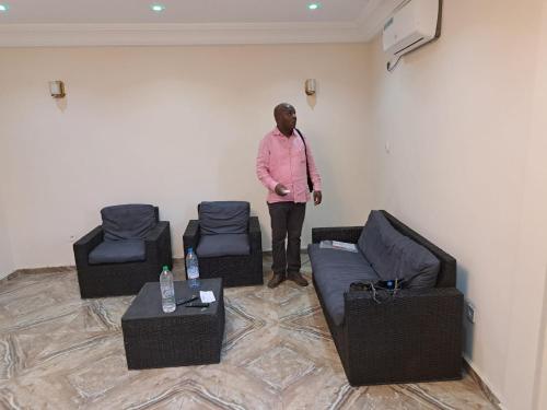 a man standing in a room with three chairs at Résidence Mado in Edéa