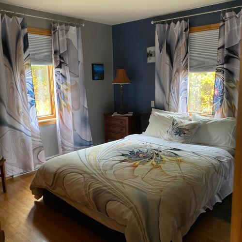 a bedroom with a bed with white sheets and windows at Le Gite de la Renarde in Saint-Félix-d'Otis