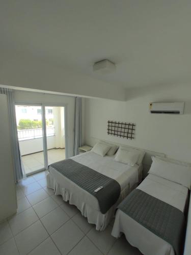 two beds in a white room with a window at Apartamento 03 suítes - Tree Bies Beach Resort - Praia de Subaúma in Entre Rios