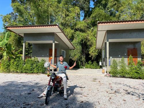a man sitting on a motorcycle in front of a house at บ้านอยู่ดีโฮมสเตย์ in Ban Hua Khao