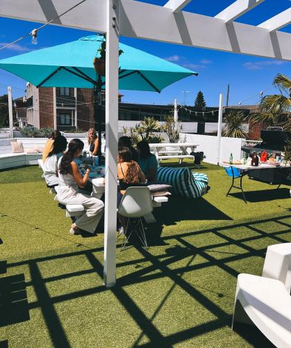 a group of people sitting at tables under an umbrella at Little Coogee Hotel in Sydney