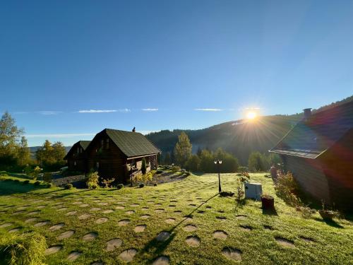 a house in a field with the sun setting behind it at Domki w górach '' Zielone Wzgórza '' okolice Karpacza in Karpacz