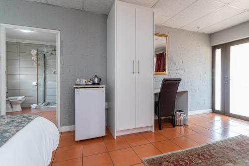 a bedroom with a bed and a desk and a bathroom at Gold Crest Guesthouse in Roodepoort