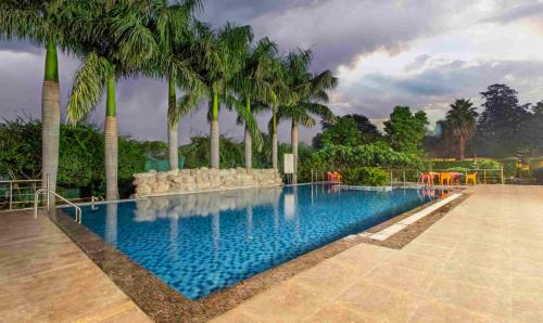 a swimming pool with palm trees in a resort at Treebo Tiger Pug Mark Resort with Pool in Rāmnagar